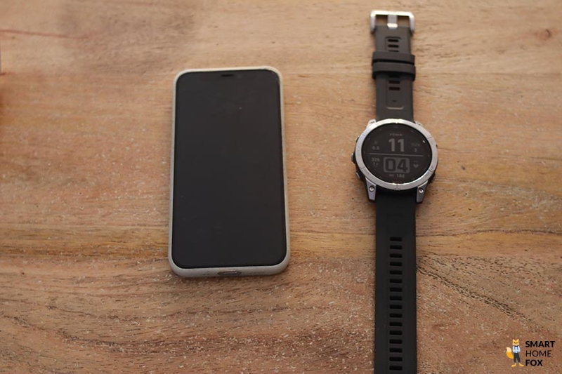 Часы Garmin Fenix 7 лежат на столе рядом с мобильным телефоном.